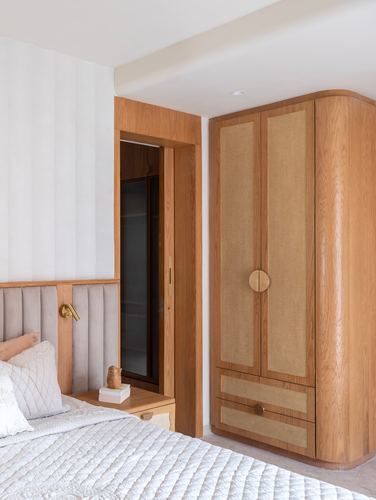 Curved wood wardrobe with cane panels beside a channel-tufted headboard bed