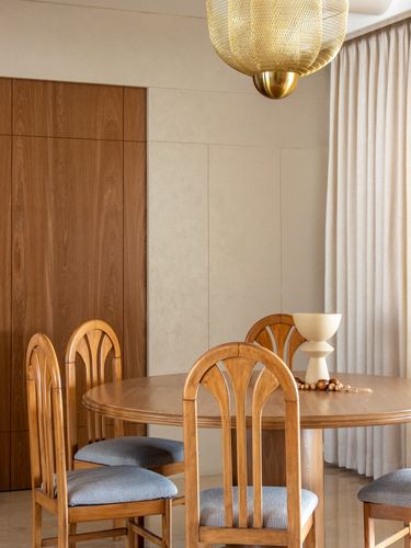 Round wood dining table with arched-back chairs under a woven brass pendant light