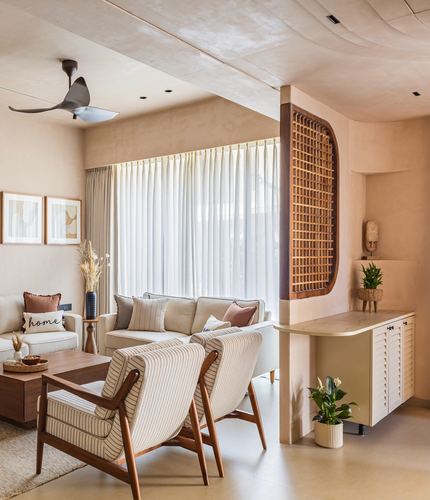 Beige living room with striped armchairs, sofa, curved wooden jaali screen, and sheer curtains