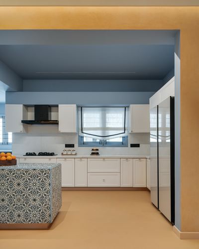 White U-shaped kitchen with blue ceiling recess and patterned tile island in mustard-walled apartment