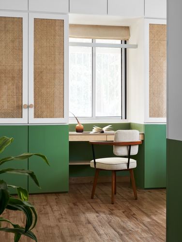 Green and white cane-front cabinetry surrounds a built-in desk with cushioned chair below a window
