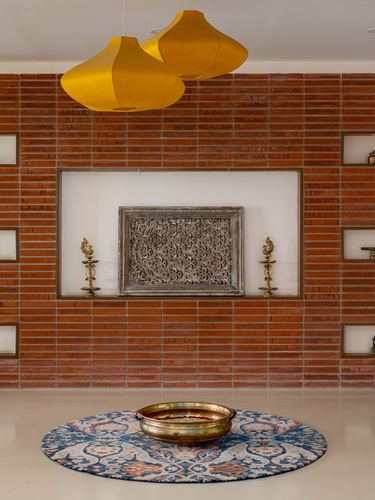 Brick-clad foyer wall with central niche, carved panel, brass lamps, and round rug with urli below