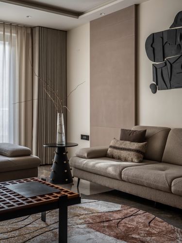 Living room corner with beige sofa, black studded side table, and dark sculptural wall art.
