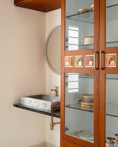Bathroom corner with stone trough sink, round mirror, and wooden glass cabinet with painted tiles