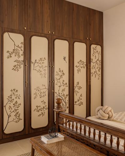 Wardrobe with painted bird and branch panels beside a carved wooden bed in a warm bedroom