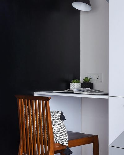 Wooden chair with patterned cushion at a small white desk against a black and white wall