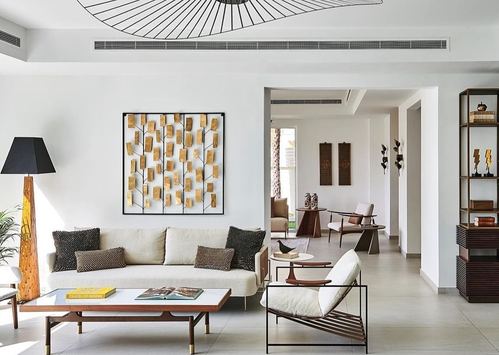 Neutral living room with gold leaf wall art, cane chair, and view through to seating beyond