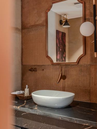 Powder room with vessel sink, black marble counter, brass fixtures, and ornate mirror against textured wall