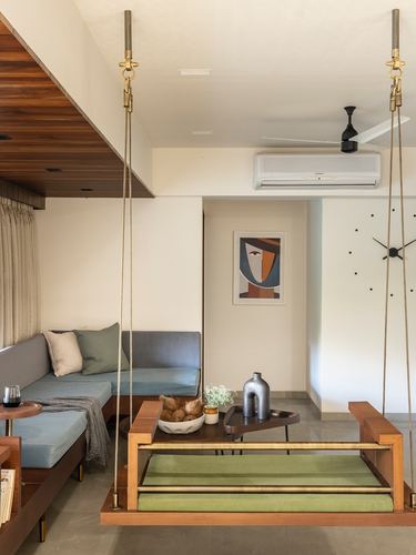 Living room with hanging wooden swing, blue sofa, framed abstract art and wall clock on cream walls