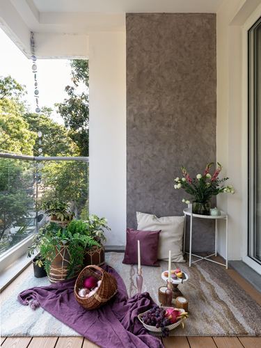Balcony with textured plaster wall, glass railing, woven planters, and mauve textiles styled with fruit and candles