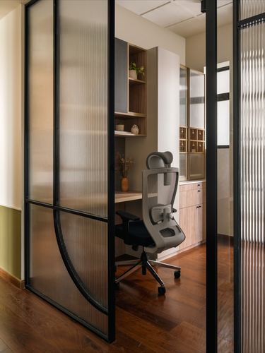 Study nook with desk and ergonomic chair seen through a curved fluted glass sliding door.