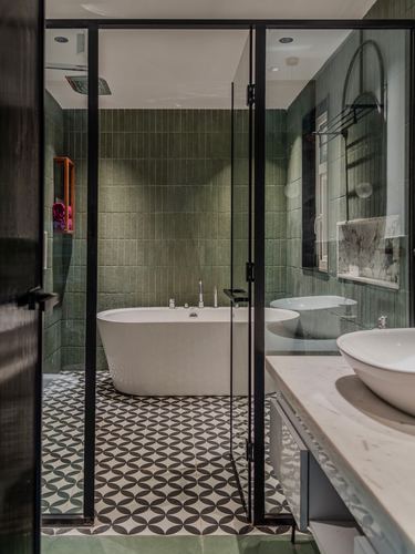 Bathroom with sage green tile, patterned floor, freestanding tub behind black glass partition