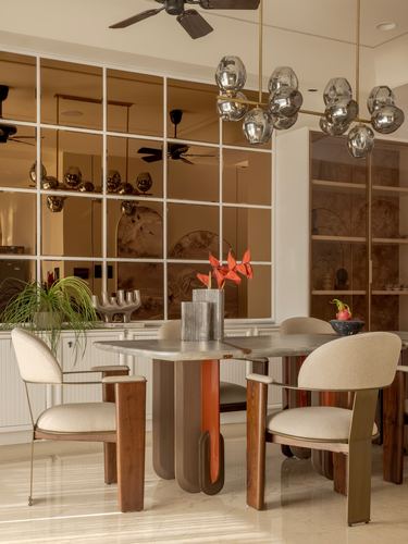 Dining room with round marble table, curved upholstered chairs, and a globe chandelier against a mirrored grid wall