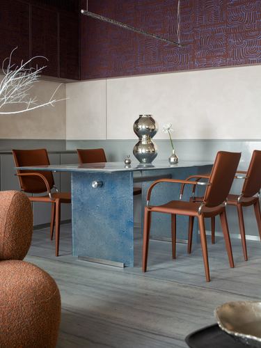 Dining area with veined stone table, orange leather chairs, and a patterned burgundy wall panel above