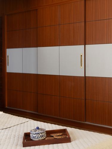 Wardrobe with wood veneer and pale panels, brass handles, tray with ceramic jar on bed foreground