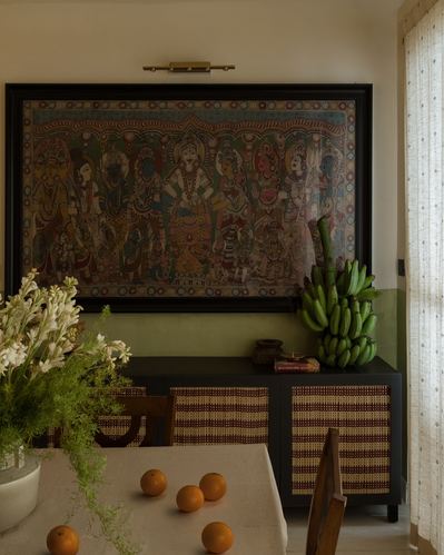 Dining nook with large traditional painting above a cane-fronted black sideboard and green wall