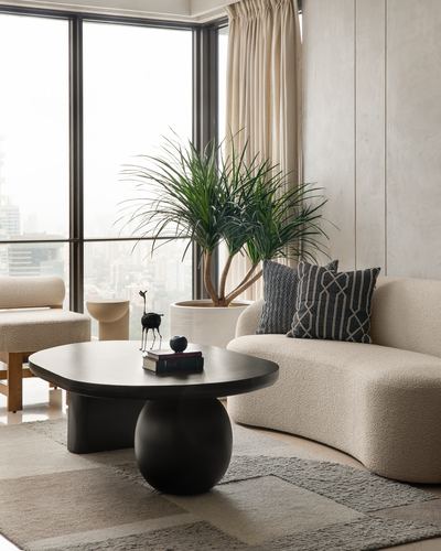 Curved cream boucle sofa beside black sculptural coffee table with city view through floor-to-ceiling windows