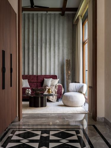 View through wooden foyer into living room with maroon sofa, fluted wall, and marble inlay floor