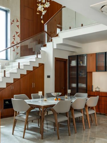 Dining area with marble-top table beneath a floating staircase with glass balustrade and wood paneling