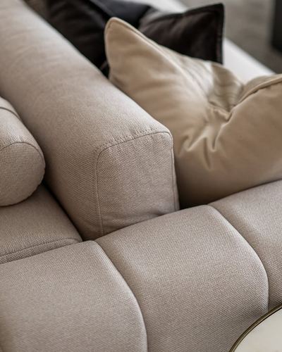 Close-up of a beige sofa with textured upholstery, bolster, and dark cushions
