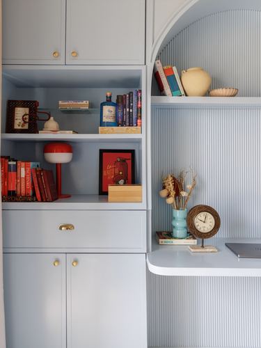 Powder blue built-in shelving with books, a red lamp, and a curved fluted desk niche