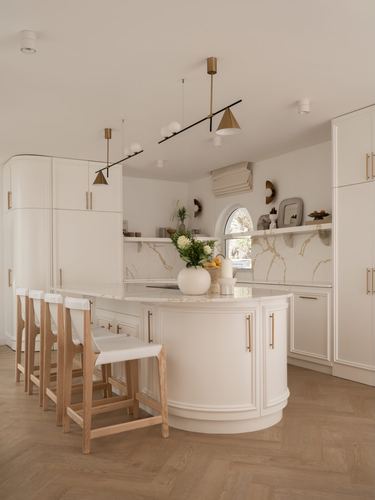 White curved kitchen island with brass pulls, arched window, and herringbone wood floor