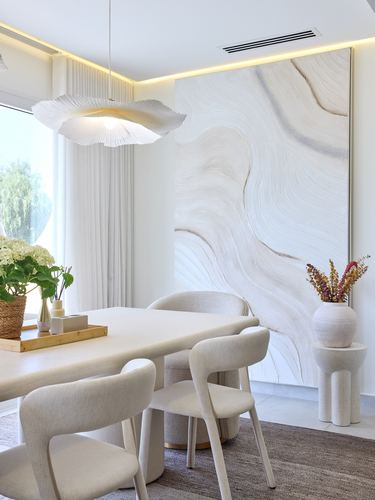 Cream dining room with boucle chairs, stone table, sculptural pendant, and large abstract wall art