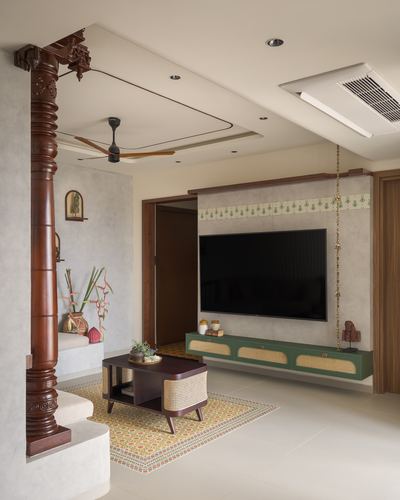 Living room with carved wooden column, patterned rug, and green cane-front TV console in a Chennai apartment