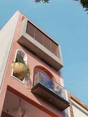 Upward view of a narrow pink multi-story facade with arched balconies and a wooden slatted screen against blue sky