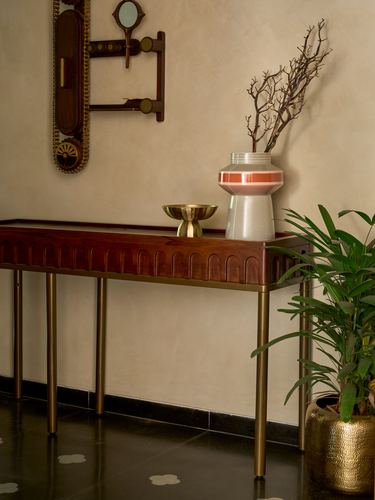 Carved wood console with brass legs holding a vase, bowl, and branches against a plaster wall