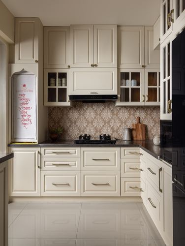 Cream-panelled L-shaped kitchen with patterned backsplash, black countertop, and glass-front upper cabinets