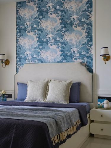 Bedroom with blue floral chinoiserie wallpaper, upholstered headboard, brass sconces and layered blue bedding