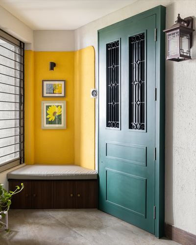 Entryway with teal paneled door, yellow accent wall, window seat with framed floral prints