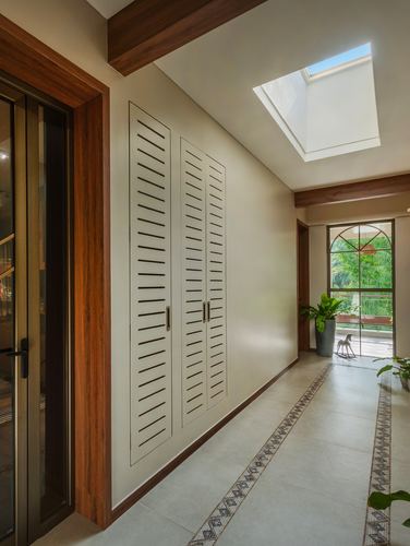 Long corridor with louvered wardrobe wall, skylight, and arched window opening to greenery