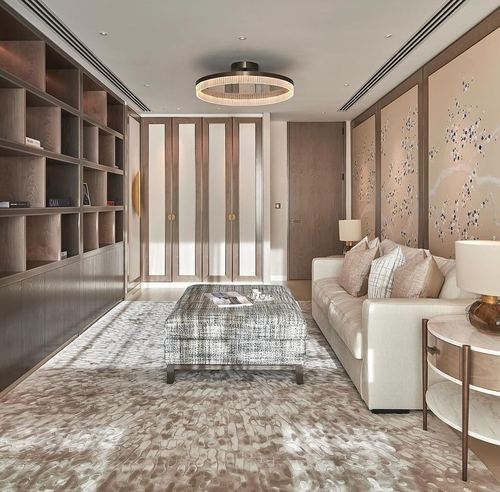 Neutral-toned living room with wood shelving, floral wall panels, cream sofa and patterned ottoman on textured rug