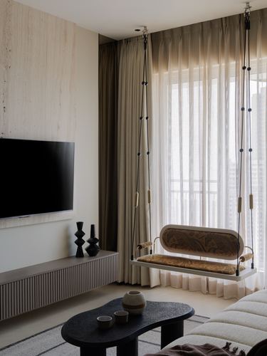 Living room with hanging swing by window, ribbed console, and wall-mounted tv against stone-clad wall