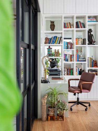 Home study nook with white bookshelves, brown leather chair, desk lamp and potted plants near glass door