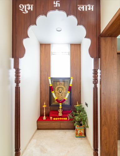 Pooja niche framed by a carved scalloped wooden arch with deity idol and garlands