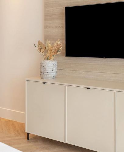 Cream sideboard with terrazzo vase beneath a wall-mounted TV on wood paneling