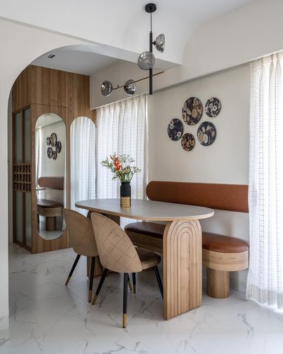 Dining nook with arched wood table, tan banquette, and decorative wall plates in Pune apartment