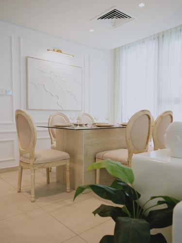 Neutral dining room with oval-back chairs around a wood-base table and glass top, textured wall art above