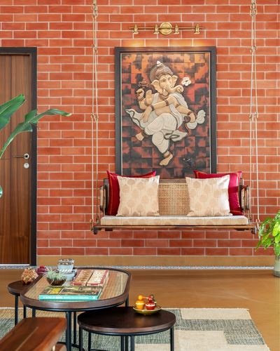 Cane swing with cushions hangs before a brick wall with a Ganesha artwork above