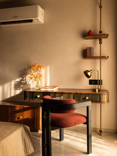 Sunlit bedroom corner with wooden desk, brass floor lamp, and rust velvet chair