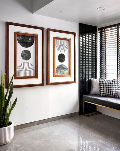 Entryway with two wood-framed artworks, snake plant, and a grey bench beside a fluted black wall.