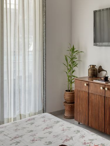 Bedroom corner with fluted wood cabinet, potted plant, brass lantern and sheer curtains