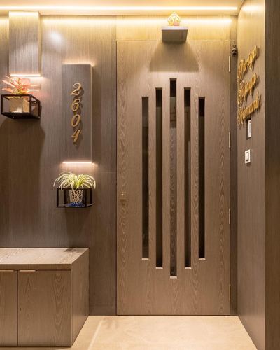 Wood-paneled apartment entrance with fluted glass-inset door and illuminated house number plaque