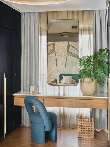 Dressing nook with arched mirror, marble-top wood console, teal curved chair, and sheer curtains