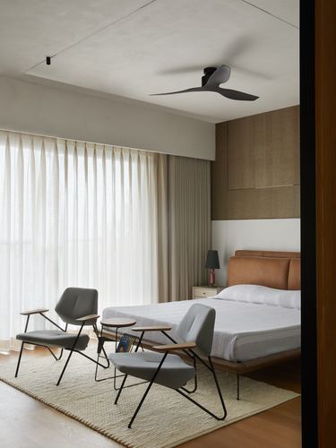 Minimalist bedroom with tan leather bed, grey lounge chairs, sheer curtains and modern ceiling fan