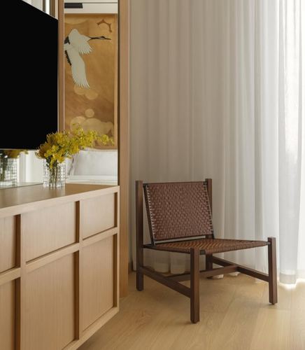 Woven leather chair by sheer curtain beside wood cabinetry and crane wallpaper reflection