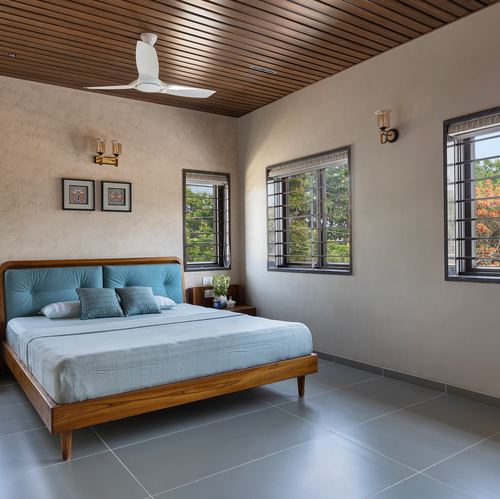 Bedroom with teal upholstered bed, wood-slat ceiling, grey tile floor and three grilled windows